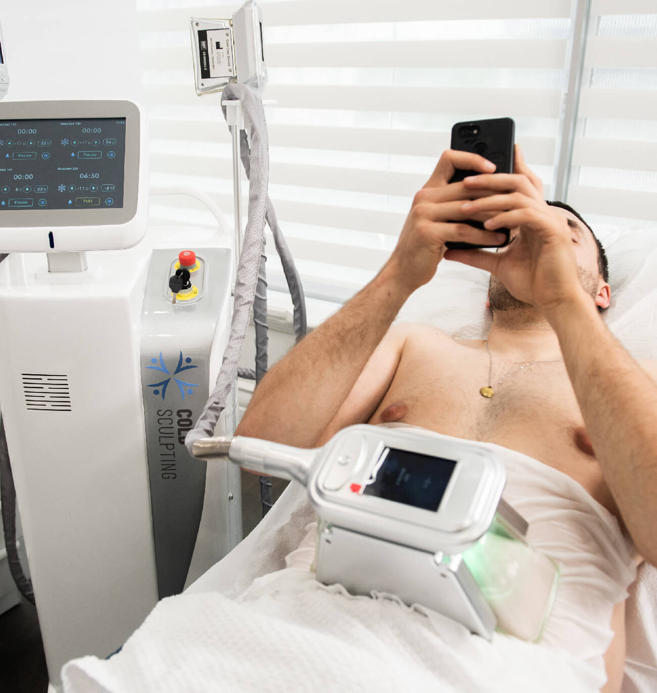 Traitement de cryolipolyse ColdSculpting appliqué sur la zone abdominale d’un client, avec affichage numérique de l’appareil pendant que le client utilise son téléphone, dans un cadre moderne et confortable.
