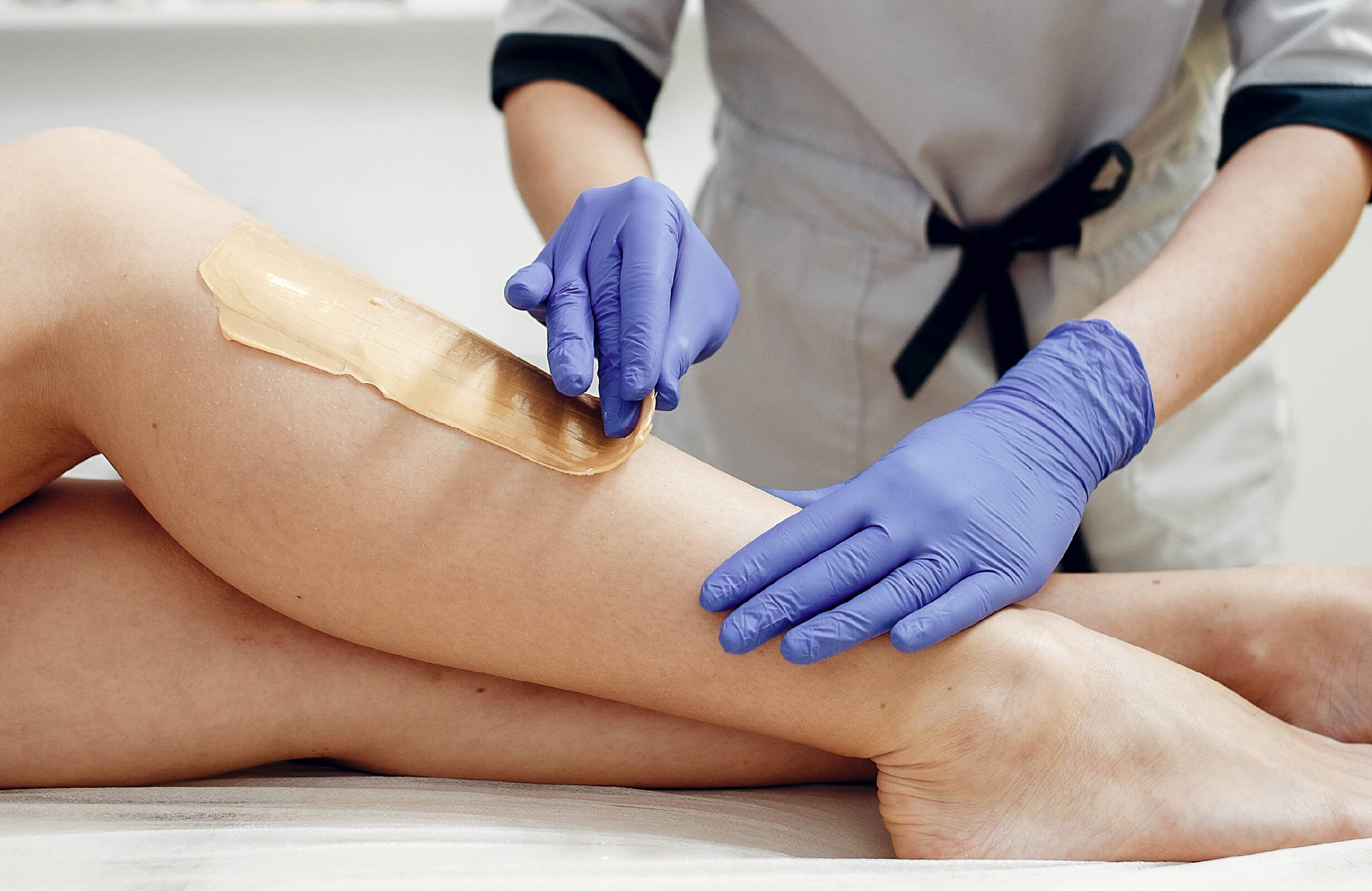 Application de cire chaude sur les jambes par un professionnel pour une épilation précise et durable.